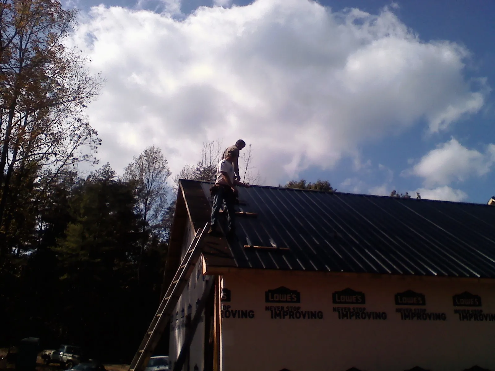 Roofer fastening dark metal panels high against a cloudy sky, from a Roof Inspection job in Portland